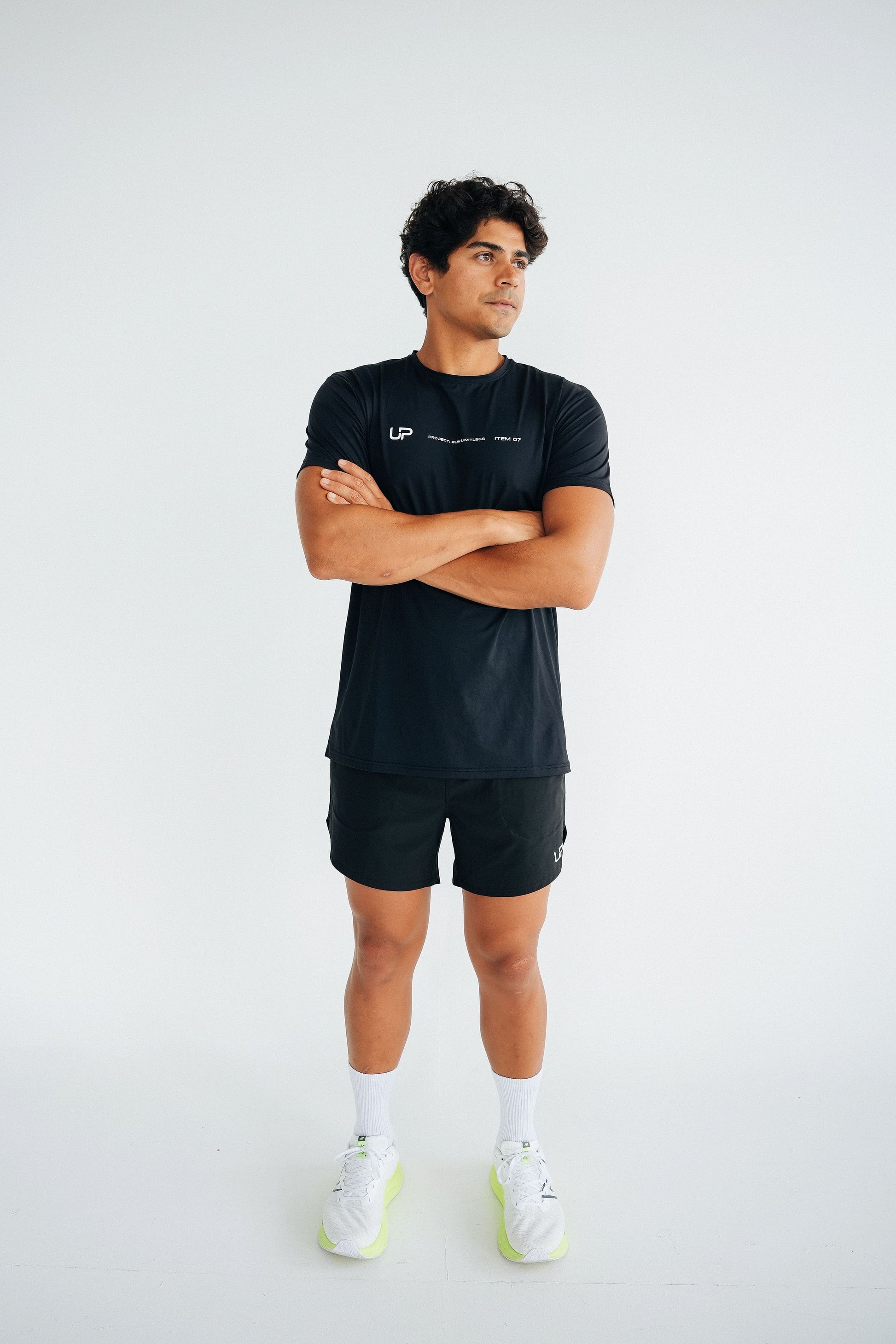 A man standing with arms crossed wearing black 'Men's Training 2-in-1 Shorts by UP Active with multiple pockets and a branded drawstring waistband.
